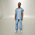 Man In Blue Scrubs Standing Full Body Against Light Colored Backdrop