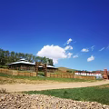 Scenic Garden Landscape with Blue Sky White Clouds Green Lawn Wooden Building and Distant Mountains