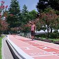 Park Landscape With Red Running Track Number Markers Pink Trees Green Grass And Clear Sky