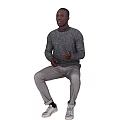 Man Sitting Against Black Background Wearing Gray Sweater Light Gray Pants And White Sneakers