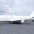White Airliner with Blue Bottom Parked on Tarmac Against Cloudy Sky and Red Tail Tip