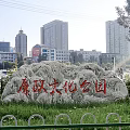 Rockery Stone with Cultural Park Inscription in Urban Green Space and Buildings