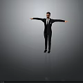 Man in Black Suit Standing with Arms Outstretched Against Grey Background
