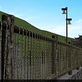 Metal Woven Fence Along Stone Path With Green Hills And Street Lights
