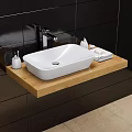 White Washbasin on Wooden Countertop with Faucet Small Bottles and Towel Against Black Tiled Wall