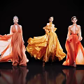 Women Showcasing Flowing Orange Yellow Long Dresses Against Black Background