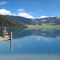 Serene Lake Landscape With Wooden Dock Person Fishing Calm Water Mountain Reflections Blue Sky Forest