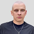 A Bald Head Man in Black Turtleneck Sweater with Silver Necklace Against Light Gray Background