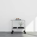 Minimalist Space with White Wall Gray Floor Metal Cart Wine Glasses Books and Green Plant