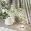 White Vase with White Flowers Green Leaves Glass Candle Holder Gold Balls Against Striped Wall