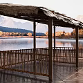 Wooden Lakeside Pavilion With Thatched Roof And Mountain Reflection At Sunset