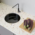 Modern Kitchen Faucet Over Black Sink On Terrazzo Countertop With Eggplants On Cutting Board