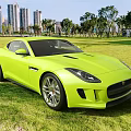Bright Yellow Jaguar Sports Car Parked On Green Grass With Tall Buildings And Trees Background