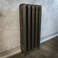 Black Decorative Cast Iron Radiator Against Gray Wall In Room With Wooden Floor