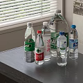 Various Brands of Bottled Water on Table by Window with Transparent Bottles and Colorful Labels