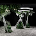 Banquet Hall With Green Plants White Flowers White Circular Decor Silver Stands And Black Backdrop