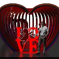 Vibrant Neon Heart Sculpture With LOVE Lettering And Cupid Design Featuring Person