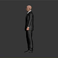 Bald Man in Black Suit and Tie Standing Against Gray Background