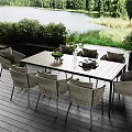 Outdoor Wicker Chairs With Wooden Table On Patio By Lake And Green Plants