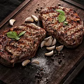 Grilled Steak on Wooden Cutting Board with Garlic Cloves Black Peppercorns Salt and Basil Leaves