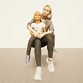 Mother and Child Sitting Together on Beige Floor in Casual Outfits with Sneakers