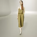 Woman Wearing Olive Green Sleeveless Jumpsuit Walking on Minimalist Gray Background with Long Hair