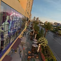 Modern Commercial Street With Glass Facades Pedestrians Outdoor Seating And Urban Skyline