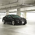 Black Bugatti Car Parked In Spacious Parking Garage With Concrete Pillars And Ceiling Lights