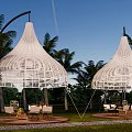 White Woven Outdoor Tents Surrounded By Palm Trees With Seating Areas
