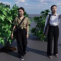Two Women Walking Outdoors With Green Plants Blue Sky and Waving Hand