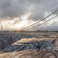 Suspension Bridge With Steel Cables Spanning Canyon Terrain Under Cloudy Sunset Sky
