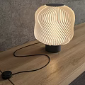Modern Wavy Lampshade Table Lamp With Warm Light On Wooden Table Against Gray Wall
