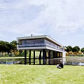 Modern Visitor Center Over Water With Pillars Surrounded By Green Trees And Blue Sky