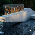 Feature Wall With SHIMA Logo Golden Letters Gray Stone Structure And Gravel Ground