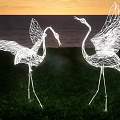 Illuminated Wire Crane Landscape Sculptures With Open Wings By Coastal Sunset Grassy Area