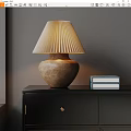 Pleated Beige Table Lamp On Black Cabinet With Stack Of Books