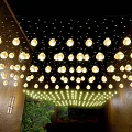 Round Shaped Decorative Lights Hanging Above Outdoor Space With Buildings And Green Plants