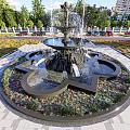 Elegant Central Fountain With Surrounding Colorful Flower Beds And Modern Glass Building Background