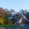 Curved Stainless Steel Sculpture in Outdoor Park with Green Trees and Shining Light