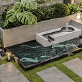 Courtyard Water Fountain with Flowing Water Lush Greenery Stone Tiles and Grass