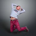 Man Kneeling Arms Raised Behind Head In Grey Green Print Top Red Pants Grey Background