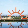Vibrant Orange Sun Shaped Sculpture with Water Reflection in Outdoor Park Setting