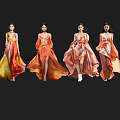 Four women in flowing orange and yellow gradient long dresses with reflections on black background