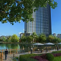Urban Park Landscape With Lake View Wooden Walkway Green Trees And High Rise Buildings
