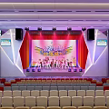 Vibrant Stage Performance With Red Curtains Performers And Audience Seats In Venue