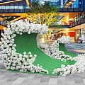 Outdoor Photo Spot With Green Wave Shaped Structure White Flowers And Modern Buildings