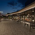 Modern Restaurant Outdoor Dining Space With Warm Lighting Green Plants And Cobblestone Pavement