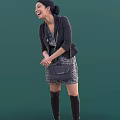 Woman Wearing Black Blazer Patterned Dress Chain Handbag and Knee High Boots on Green Background