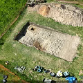 Top Down Aerial View Of Outdoor Archaeological Excavation Trench On Grassy Site With Working Tools