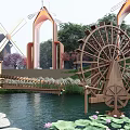 Wooden Waterwheel Sculpture in Park Setting With Pond Lotus Leaves Arched Structures And Windmill
